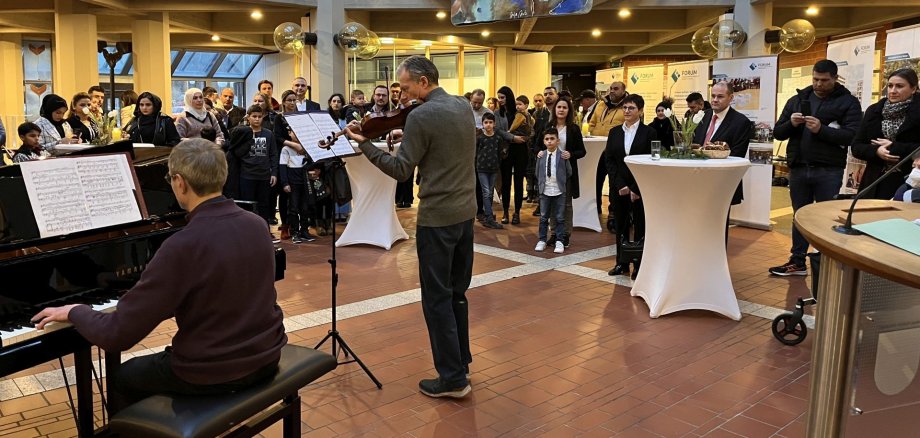 Im Vordergrund ein Geige- und ein Violinspieler, im Hintergrund rund 30 Personen bei der Einbürgerungsfeier im Foyer des Kreishauses.