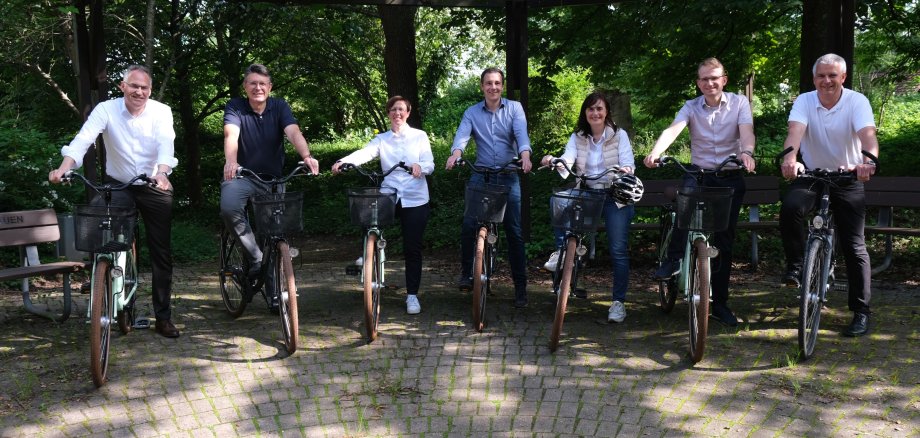 Landrat Dietmar Seefeldt sowie die Bürgermeisterinnen und Bürgermeister der sieben Verbandsgemeinden im Landkreis (Ausnahme: Offenbach an der Queich) stehen nebeneinander, jeder hat ein Fahrrad.