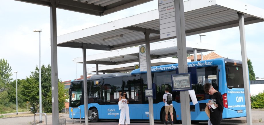 Ein blauer Bus am Busbahnhof, davor wartende Fahrgäste.