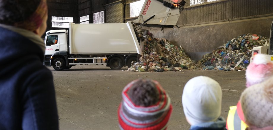 Während einer Führung im Wertstoffwirtschaftszentrum Nord in Edesheim beobachten Schulkinder und eine Lehrerin ein Müllfahrzeug, das seine Ladung auskippt.