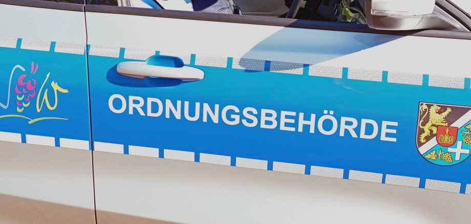 Auf einer Autotür steht auf blauem Untergrund in Versalien Ordnungsbehörde. Links davon ist das Logo des Landkreises SÜW, rechts davon das Kreiswappen.