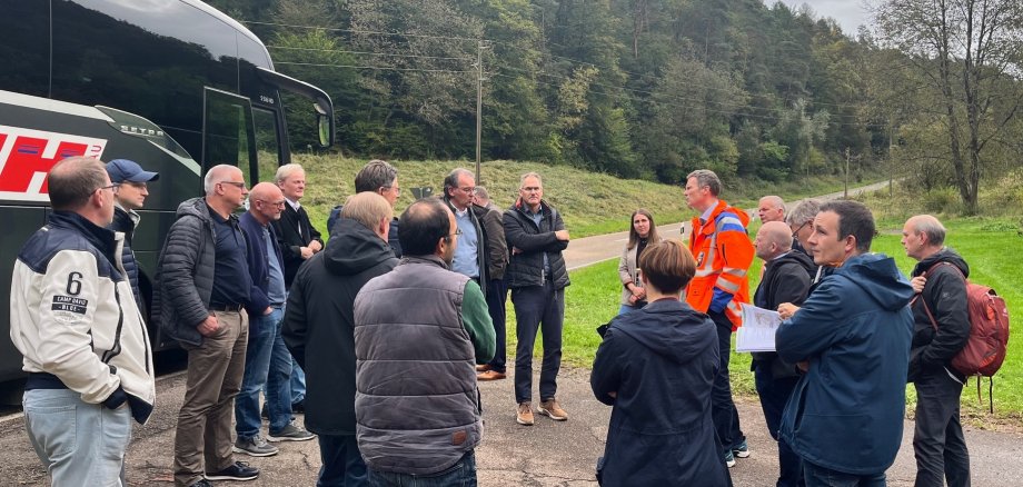 Mitglieder des Kreisausschusses stehen in einer Gruppe zusammen und hören den Ausführungen eines Vertreters des Landesbetriebs Mobilität zu. Der Austausch findet an einer Straße im Grünen statt, im Rahmen einer Rundfahrt durch den Landkreis Südliche Weinstraße, um den Zustand der Kreisstraßen zu begutachten.